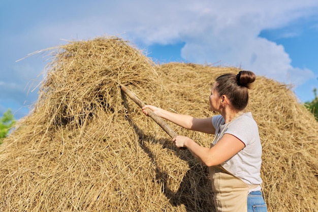 Mujer agricultora trabajando con pasto seco, paja. Pajar, fondo de cielo azul de campo