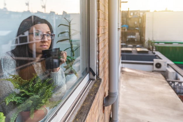 Mujer aislada en casa sola y mirando por la ventana