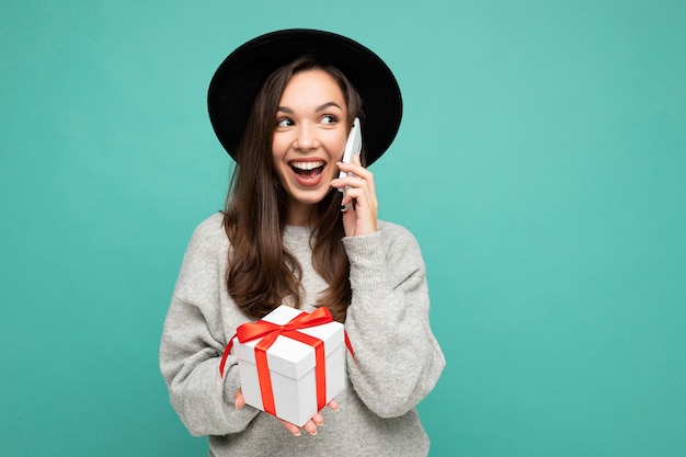 mujer aislada sobre fondo colorido pared vistiendo ropa casual elegante con caja de regalo y mirando hacia el lado.