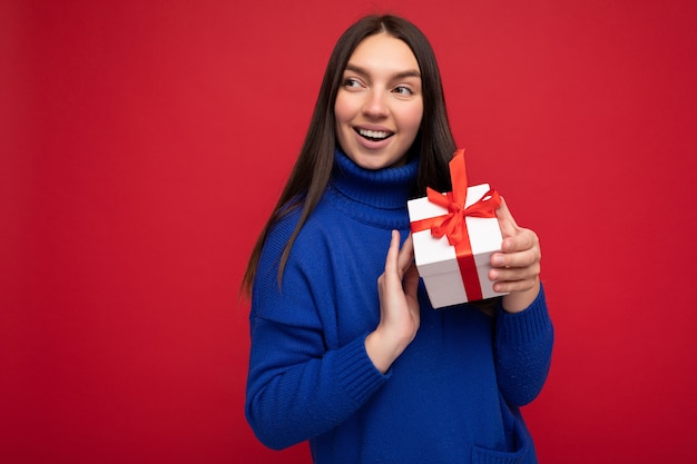 mujer aislada sobre pared colorida vistiendo ropa casual elegante con caja de regalo y mirando hacia el lado.