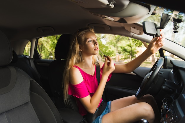 Mujer ajustando el espejo del coche para maquillaje