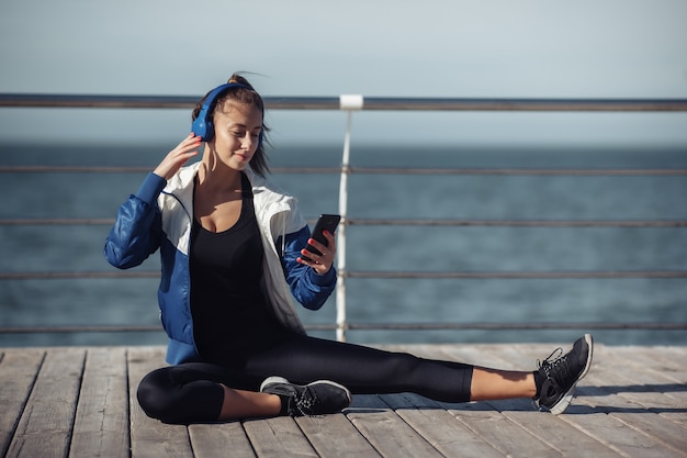 Mujer de ajuste relajado en ropa deportiva con auriculares elige música de un teléfono inteligente para entrenar