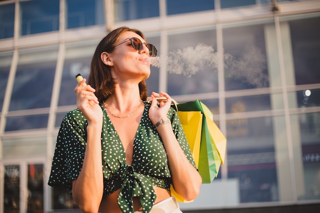 Mujer al atardecer con coloridas bolsas de la compra y fumar café disfrutando de cigarrillos electrónicos