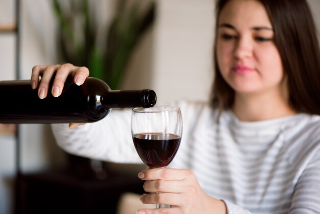 Mujer alcohólica embarazada está vertiendo vino de una botella en un vaso y bebiendo.