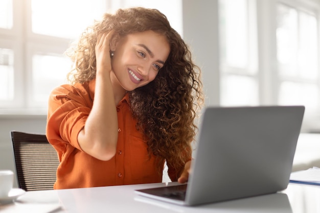 Mujer alegre al lado de la computadora portátil tocando su cabello