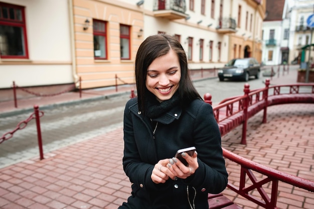Mujer alegre atractiva joven que usa el teléfono en la calle en la ciudad