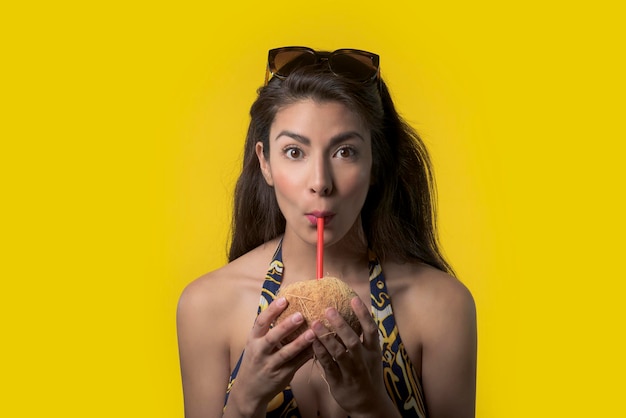 mujer alegre bebiendo agua de coco en un concepto de vacaciones de verano de fondo amarillo