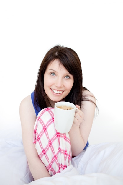 Mujer alegre bebiendo café sentado en la cama