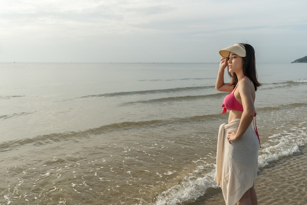 Mujer alegre en bikini de pie en la playa del mar