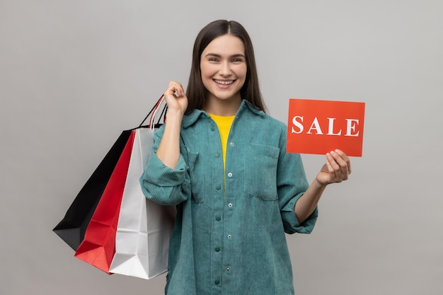 Mujer alegre con cabello oscuro con tarjeta de venta y bolsas de compras feliz con precios bajos