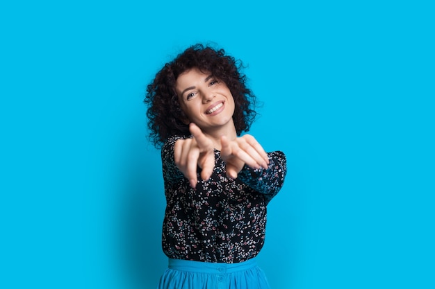 Mujer alegre con cabello rizado apunta a la cámara mientras posa