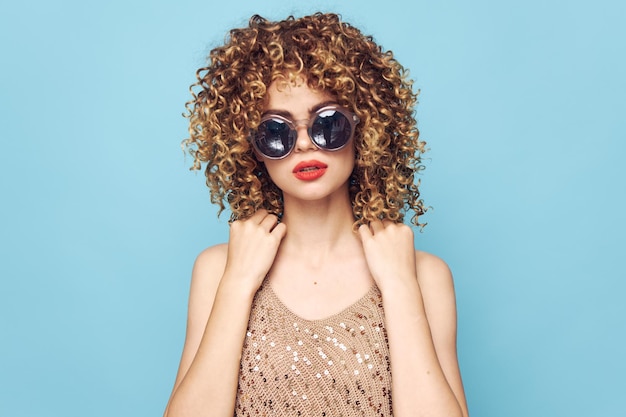 Mujer alegre Cabello rizado, gafas redondas y oscuras Estilo elegante Maquillaje brillante Fondo azul