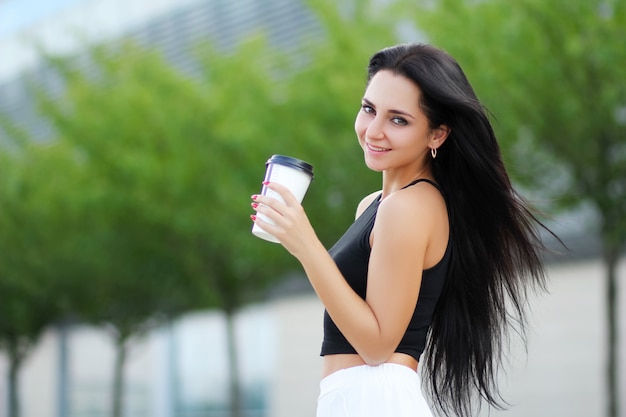 Mujer alegre en la calle bebiendo café de la mañana en el sol