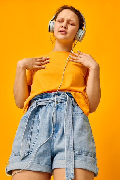 Mujer alegre camiseta amarilla auriculares entretenimiento música diversión fondo amarillo inalterado