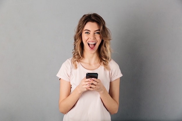 Mujer alegre en camiseta con smartphone y sobre gris