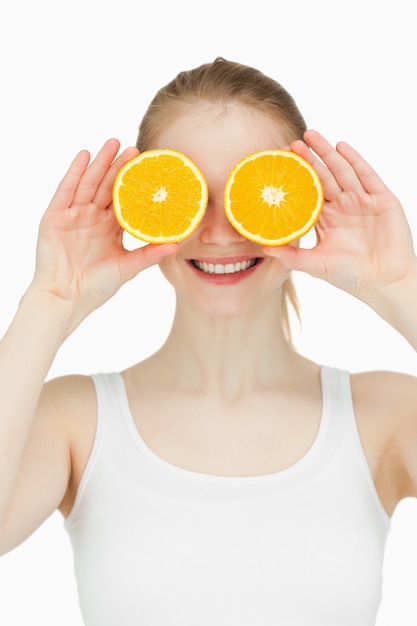 Mujer alegre colocando naranjas en los ojos