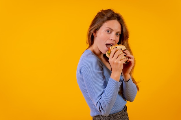 Mujer alegre comiendo un sándwich en un fondo amarillo comida sana y vegetariana