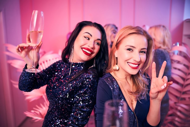 Mujer alegre con una copa de champán mirando a su amiga