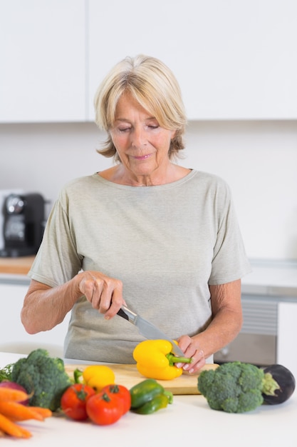 Mujer alegre cortando un pimiento amarillo