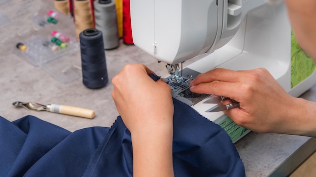 Mujer alegre cosiendo mientras se sienta en su lugar de trabajo en el taller de moda