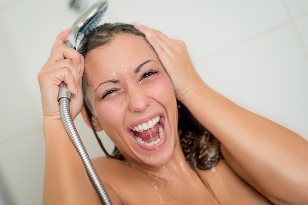 Foto mujer alegre de la ducha que se lava la cara y el cabello mientras se ducha bajo el cabezal de la ducha.