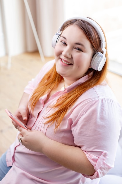 Mujer alegre encantada sentada con su teléfono inteligente mientras escucha música