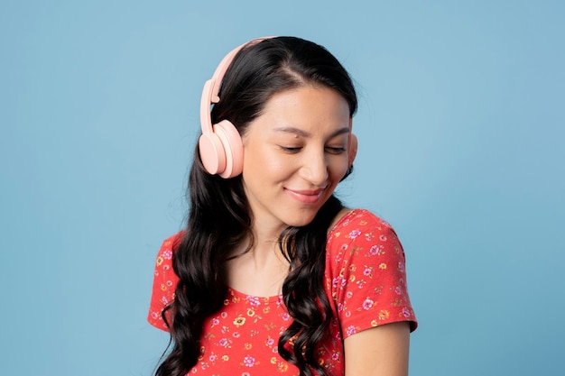 Mujer alegre escuchando música con un auricular sobre fondo azul.