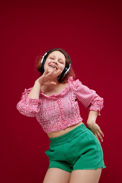 mujer alegre escuchando música con auriculares bailando sobre un fondo rojo inalterado. foto de alta calidad