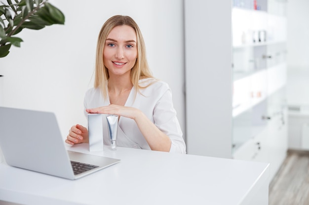 Mujer alegre esteticista usando laptop en salón de belleza