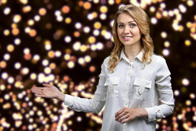 Mujer alegre feliz en camisa de oficina formal anunciando algo sobre fondo abstracto de Navidad.