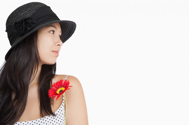 Mujer alegre con flor mirando lejos con un sombrero