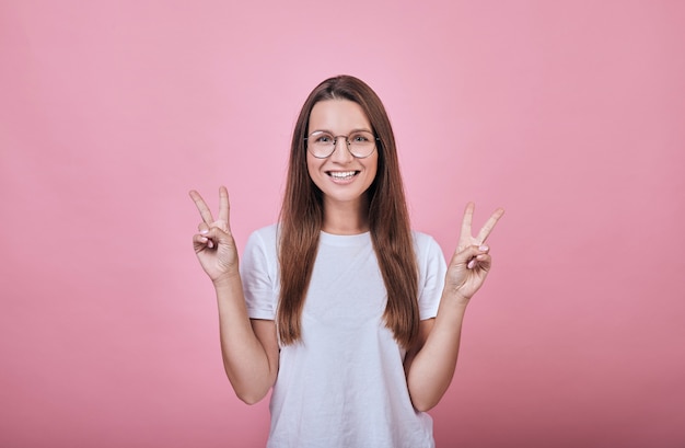 Mujer alegre con gafas y camiseta blanca muestra dedos paz