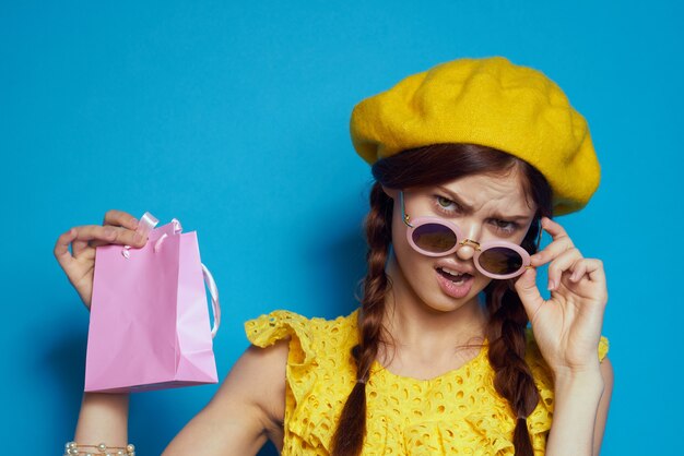 Mujer alegre con gafas de sol posando fondo azul de moda de compras