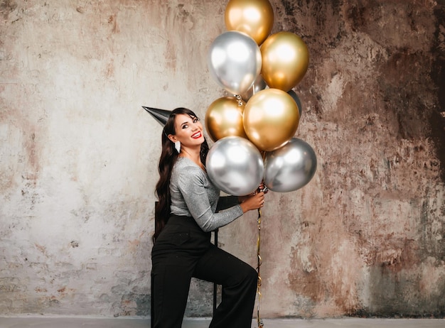 Una mujer alegre con globos se ríe una joven morena con el pelo largo celebra su cumpleaños globos de helio