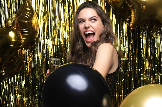 Mujer alegre con globos riendo sobre fondo dorado.