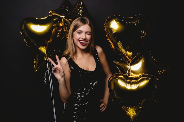 Mujer alegre con globos riendo sobre fondo negro.