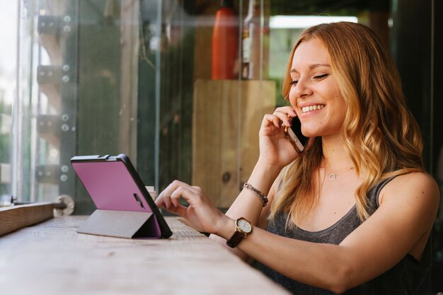 Mujer alegre hablando con su teléfono móvil y utilizando tecnología moderna