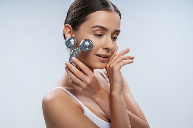 Mujer alegre haciendo masaje facial con dispositivo moderno