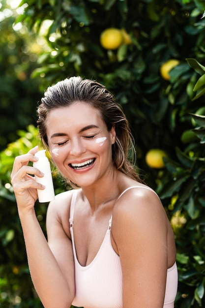 Mujer alegre y hermosa aplicando crema hidratante o bloqueador solar en su piel facial