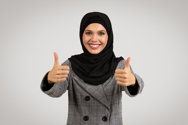 Mujer alegre con hijab levantando los pulgares en el traje