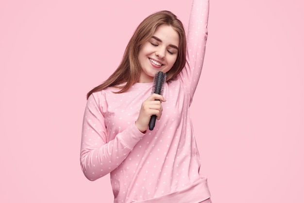 Mujer alegre imitando cantar con cepillo para el pelo