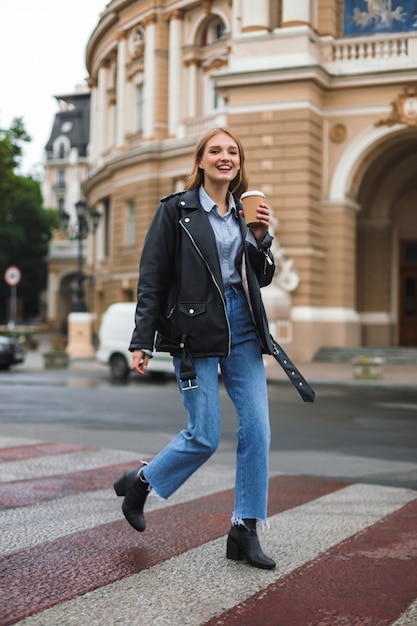 Mujer alegre joven en chaqueta de cuero y jeans felizmente