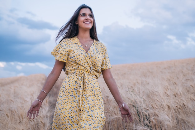 Mujer alegre joven disfrutando de la naturaleza mientras camina por un campo de trigo.