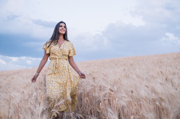 Mujer alegre joven disfrutando de la naturaleza mientras camina por un campo de trigo.