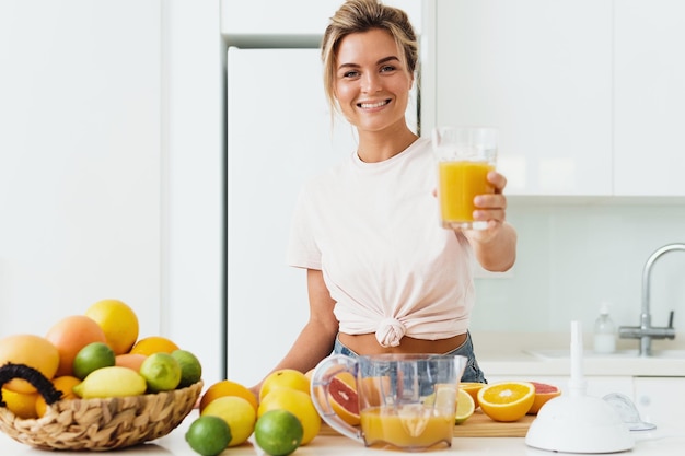 Mujer alegre joven con gran vaso de jugo de naranja fresco