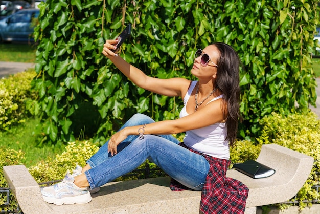 Mujer alegre joven toma selfie de manos con teléfono mientras está sentado en el parque