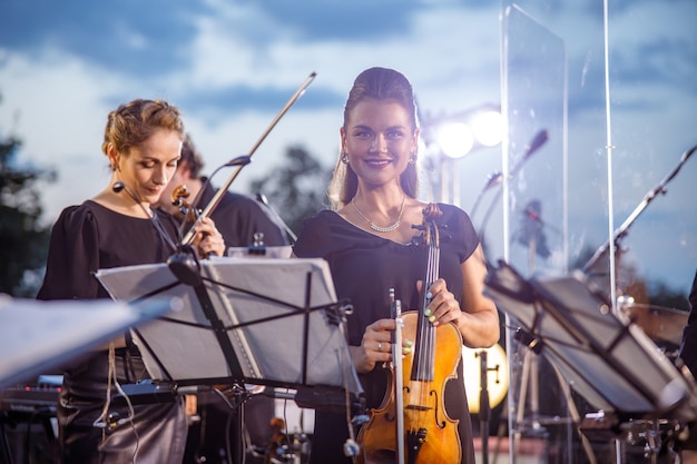 Mujer alegre jugador de violín tocando en la orquesta al aire libre