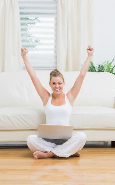 Mujer alegre levantando las manos durante el uso de la computadora portátil