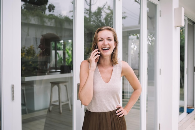 Mujer alegre llamando al teléfono móvil y riendo en el patio