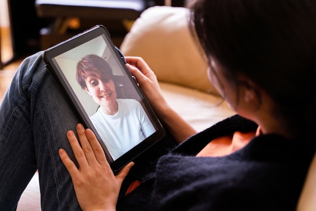 Mujer alegre llamando a un amigo con dispositivo de tableta. concepto de distancia social en aislamiento de cuarentena en casa. tecnología personas estilo de vida en la casa.